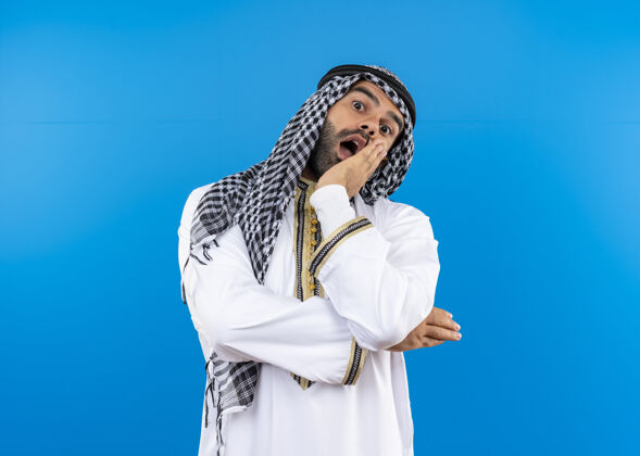 站身着传统服装的阿拉伯男子站在蓝色的墙壁上惊讶不已看惊人惊喜