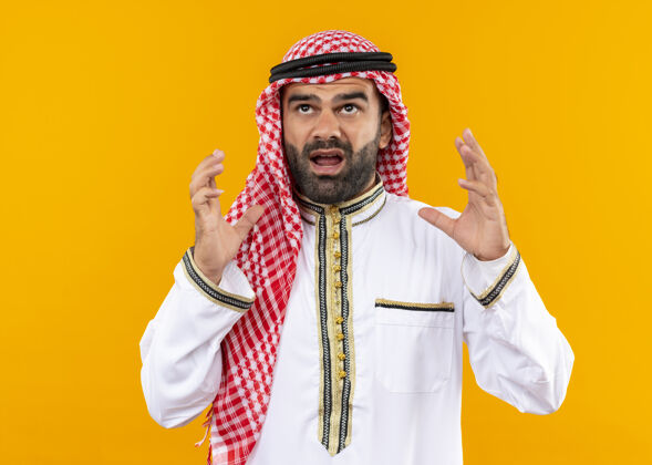 手沮丧的阿拉伯商人穿着传统服装站在橙色的墙上高声喊叫沮丧阿拉伯语穿