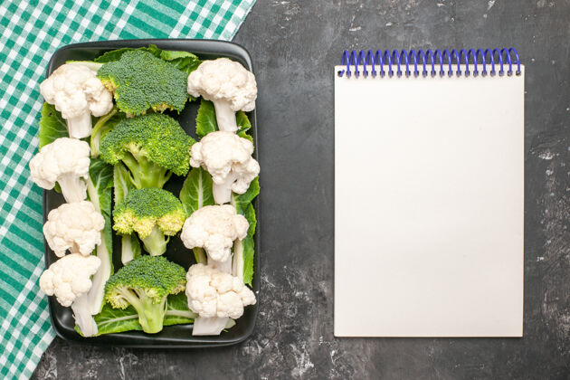 花椰菜在绿色和白色方格餐巾上的黑色矩形板上俯视生西兰花和花椰菜在黑暗的表面上的笔记本蔬菜方格美食