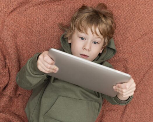 平板电脑小男孩在床上使用平板电脑的俯视图设备娱乐男孩