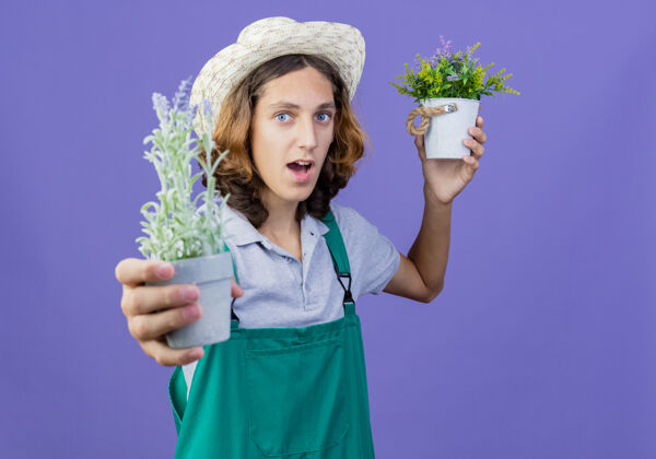 花园年轻的园丁 穿着连体衣 戴着帽子 微笑着展示盆栽植物站立植物帽子