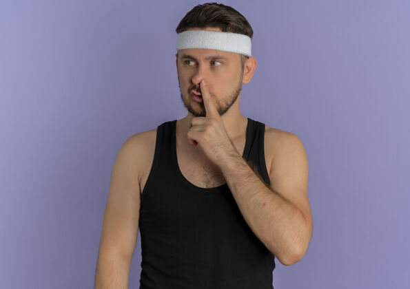 男性戴着头巾的年轻健身男子用手指捂住鼻子站在紫色的墙上头带年轻站着