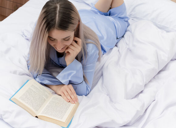 卧室穿着蓝色睡衣躺在床上的年轻漂亮女人年轻书美丽
