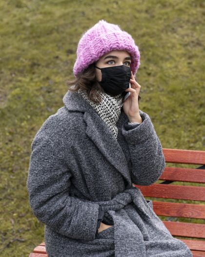 人类城里戴着医用口罩的女人在长凳上打电话流行病冠状病毒个人