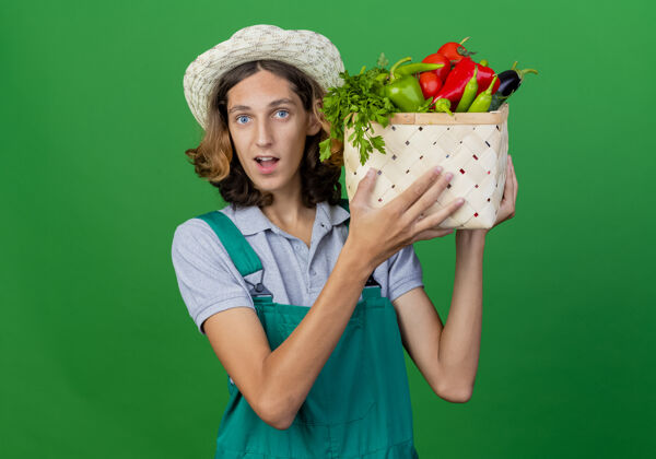穿着年轻的园丁穿着连体衣戴着帽子拿着装满新鲜蔬菜的箱子板条箱年轻男人