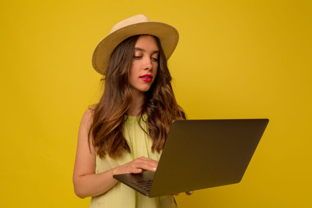 表情一个戴着长波浪发帽子的时髦女孩在隔离墙上用笔记本电脑拍摄的特写照片兴奋欢呼好