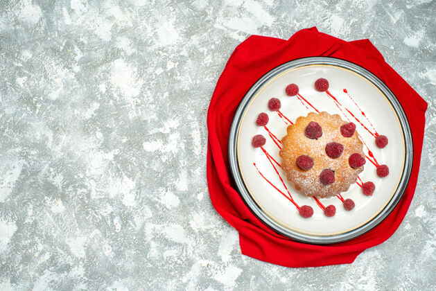 玫瑰俯瞰白色椭圆形盘子上的浆果蛋糕 灰色表面上的红色披肩 自由空间盘子花视图