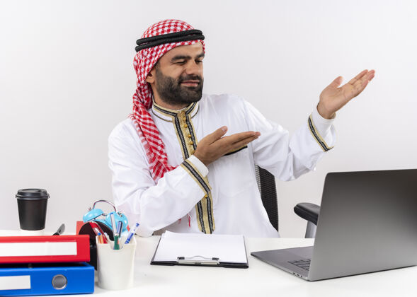 指尖身着传统服装的阿拉伯商人坐在桌子旁 手提电脑指着办公桌旁的一边穿工作壁板