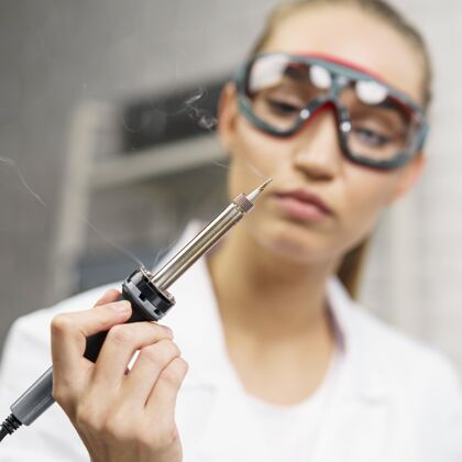 科学家带烙铁和安全眼镜的女技师的前视图研究实验室女
