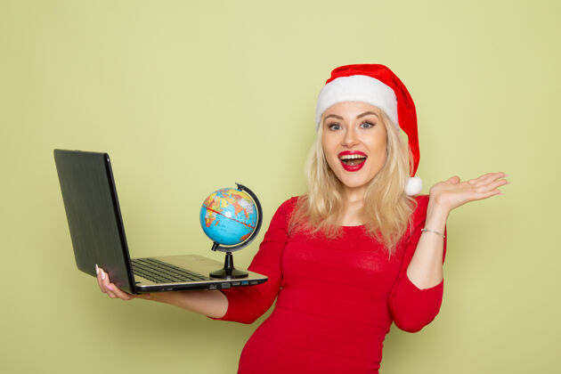 漂亮正面图美丽的女性手持小地球仪和笔记本电脑在绿色的墙上圣诞色雪景新年情感雪圣诞节漂亮的女人