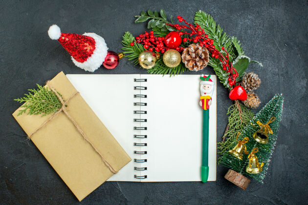 信封顶视图圣诞心情与杉木树枝圣诞老人帽子圣诞树礼品盒笔记本上的黑暗背景圣诞心情笔记本帽子