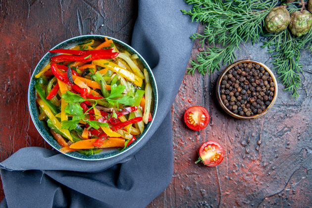 碗顶视图蔬菜沙拉在碗黑胡椒冷杉枝群青蓝色披肩在暗红色的桌子上蔬菜餐胡椒粉