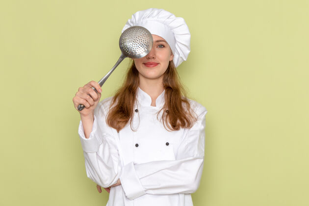 银色身穿白色厨师服的女厨师手持大银勺 在绿色墙上微笑着思考烹饪女厨师套装