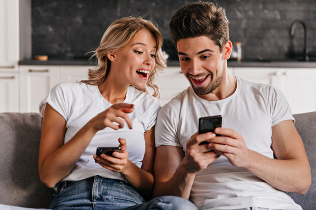 情侣一对微笑的夫妇坐在沙发上拿着手机可爱的年轻女子拿着智能手机周末室内妻子