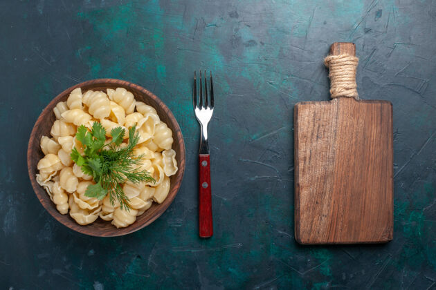 刀顶视图煮熟面团面食与绿色内板在黑暗的桌子上餐厅盘子面团