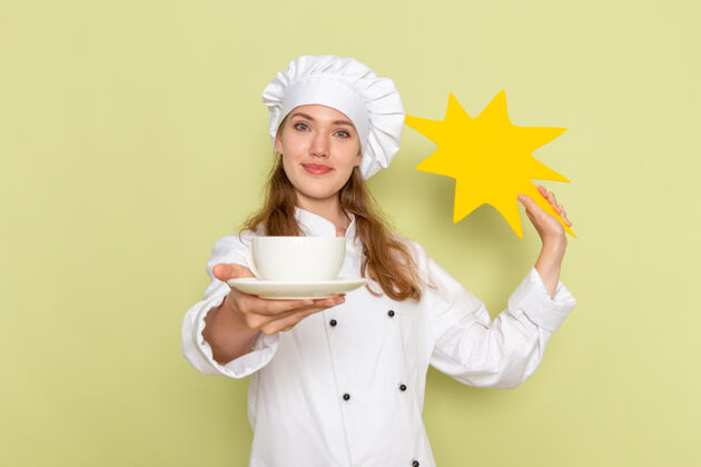 烹饪身穿白色厨师服的女厨师正对着绿色墙上的黄色标牌和盘子人食物帽子