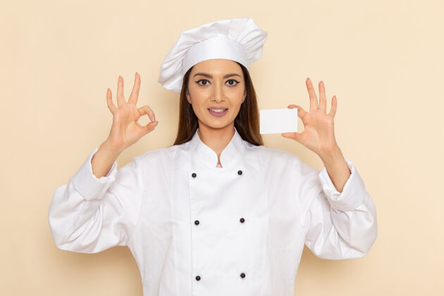 快乐身穿白色厨师服的年轻女厨师手持白色塑料卡站在浅白的墙上专业套装肖像