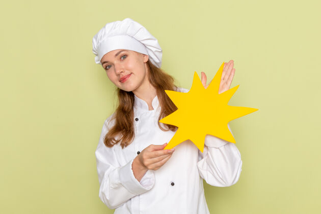 人身着白色厨师服的女厨师正对着绿色墙上挂着微笑的黄色招牌前面女烹饪