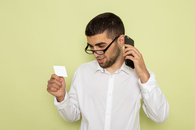 商业身穿白衬衫的男上班族手持名片 在绿墙上打电话的正面图手持电话工人