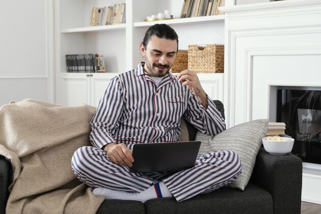 室内穿着睡衣的男人在笔记本电脑上玩得很开心工作区技术年轻人