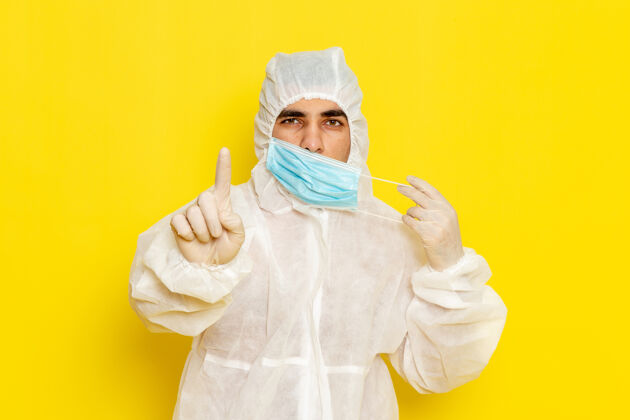 科学身穿特殊防护服的男科学工作者在黄色墙壁上脱下面具的正面图面罩特殊套装