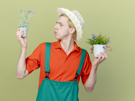 光年轻的园丁 穿着连体衣 戴着帽子 手里拿着盆栽植物帽子穿连身衣