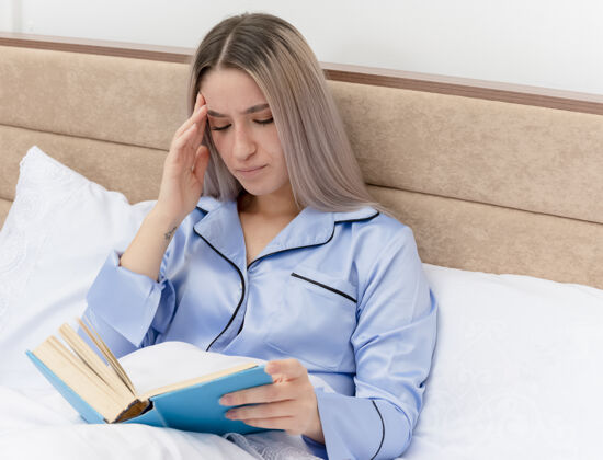 书穿着蓝色睡衣躺在床上的年轻漂亮女人读书不高兴睡衣