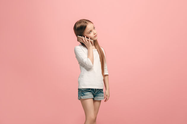 年轻快乐的少女站着 微笑着用手机在时尚的粉红色工作室幸运成人人类