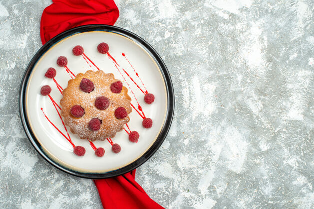 视图俯瞰白色椭圆形盘子上的浆果蛋糕 灰色表面上的红色披肩 自由空间盘子粉末餐具