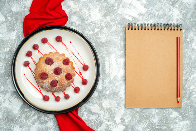 午餐俯视图白色椭圆形盘子上的浆果蛋糕红色披肩红色铅笔在灰色表面的记事本上盘子粉末盘子