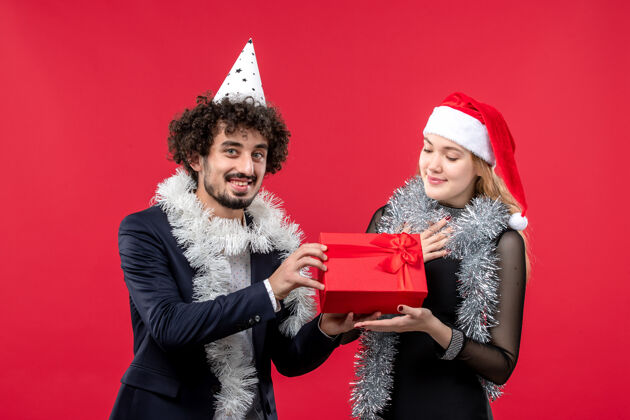色彩正面图：年轻夫妇带着礼物在红墙上庆祝圣诞爱情派对的颜色肖像快乐圣诞