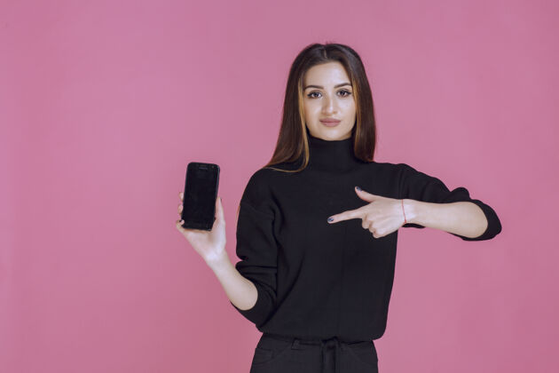 姿势穿着黑色毛衣的女人拿着一部智能手机指着它成人年轻人设备