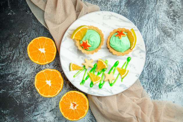 馅饼顶视图小馅饼与绿色糕点奶油和柠檬片在盘子上米色披肩在黑暗的桌子上切橘子盘子新鲜水果