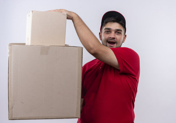 盒子年轻的送货员穿着红色制服 戴着帽子 手里拿着大纸箱 看上去既惊讶又惊奇站着送货惊喜