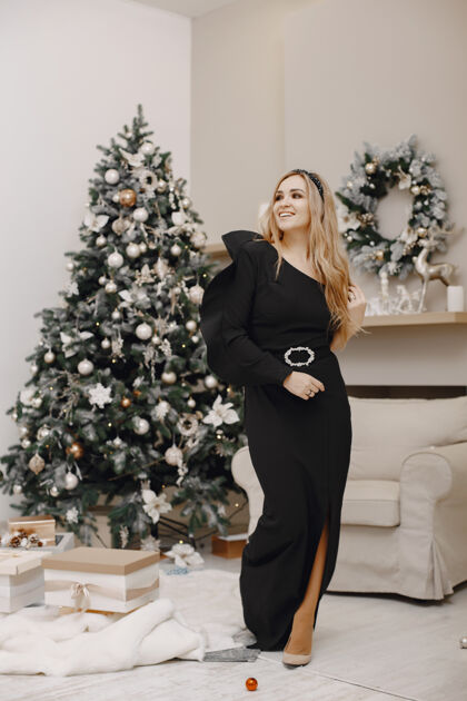 卷发圣诞树旁的优雅女士房间里的女人穿着优雅黑色连衣裙的家人连衣裙魅力夜晚