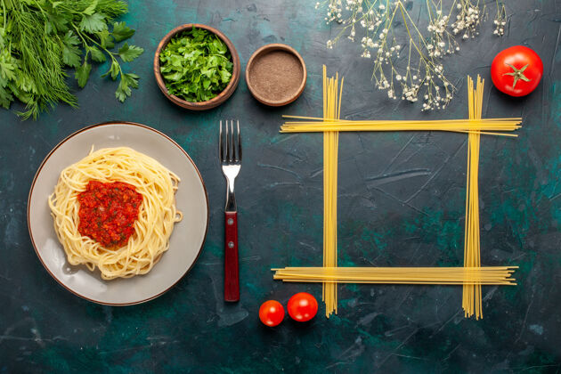 生的俯视图：蓝色表面上有番茄酱肉末和不同调味料的意大利熟面食酱汁肉菜肴