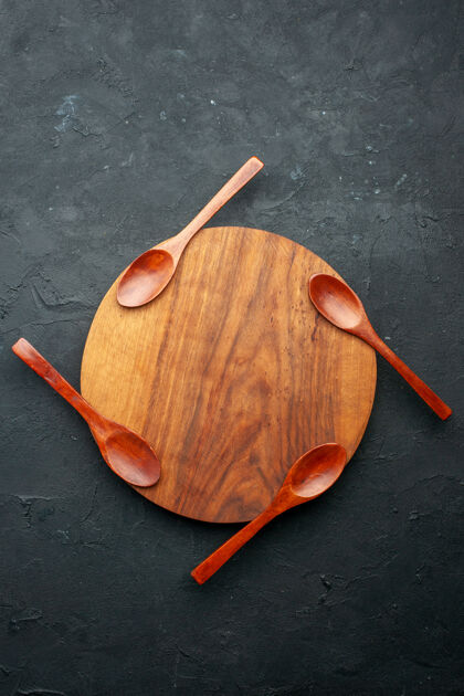 木制顶视图四个勺子放在黑暗的桌子上的圆板上木头季节勺子