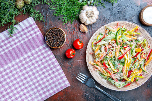 餐厅顶视图蔬菜沙拉在盘子桌布叉子盐和黑胡椒大蒜西红柿在暗红色的桌子上桌布肉叉子