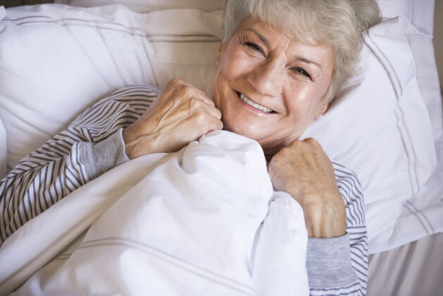 微笑睡在床上的漂亮的老太太躺下舒适卧室