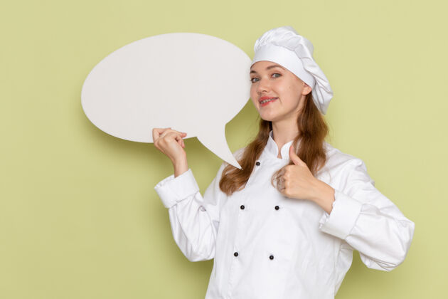 套装身着白色厨师服的女厨师手持绿色墙上巨大的白色标牌的正面视图前面烹饪人