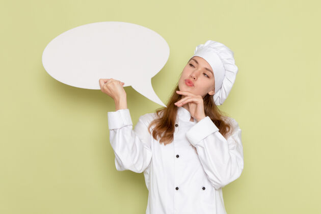 持有身穿白色厨师服的女厨师手持大牌子 在绿色墙上思考穿微笑大
