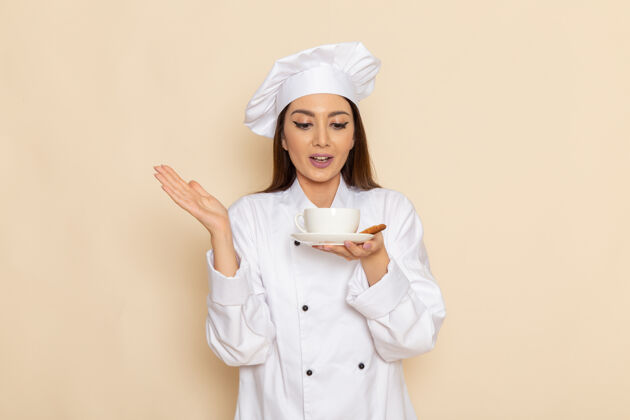 医生身穿白色厨师服的年轻女厨师正拿着一杯咖啡站在浅白的墙上烹饪厨房工作