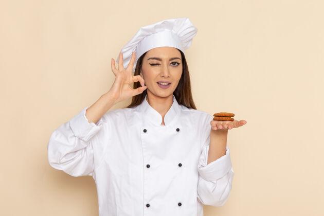 套装身穿白色厨师服的年轻女厨师手持饼干 在浅白的墙上眨眼年轻专业前面