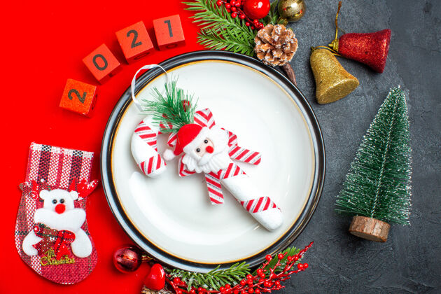 容器新年背景的特写镜头与餐盘装饰配件杉木枝和数字圣诞袜在一个红色餐巾旁边的圣诞树在一个黑色的桌子上树枝袜子餐巾