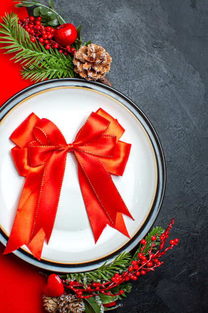 风景新年背景顶视图用红丝带放在餐盘上餐具套装装饰配件杉木树枝旁边的一个礼物上 一张红色餐巾放在一张黑色的桌子上圣诞餐巾树枝