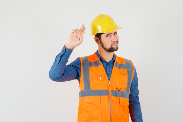 头盔年轻的建筑工人用手和手指在衬衫里做手势手年轻人衬衫