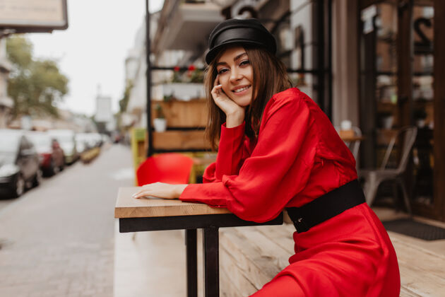 时尚女孩23岁的法国女孩坐在街上的咖啡馆里摆姿势优雅的女士穿着宽袖红裙子的舒适镜头花式女孩连衣裙
