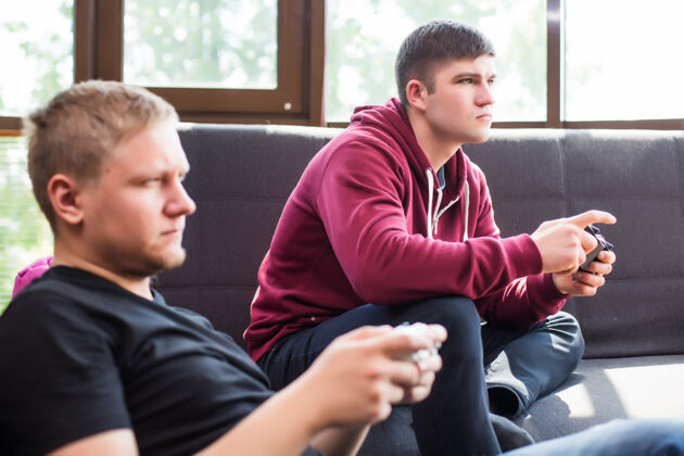 友谊两个快乐的年轻人坐在沙发上玩电子游戏沙发竞争坐
