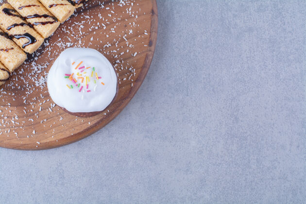 盘子一块用甜木棍做成的木板 上面放着奶油蛋糕和五颜六色的花洒甜食碗橱蛋糕食物