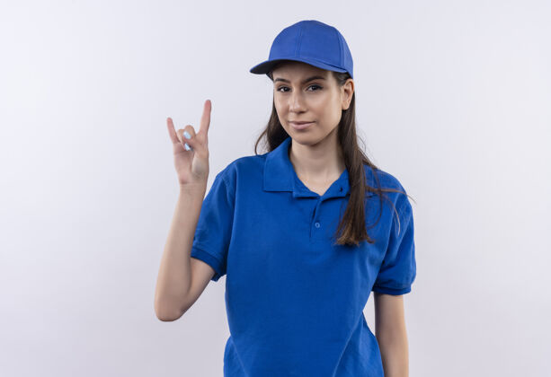 显示身穿蓝色制服 戴着帽子的年轻送货女孩自信地用手指展示摇滚乐的象征蓝色女孩交付